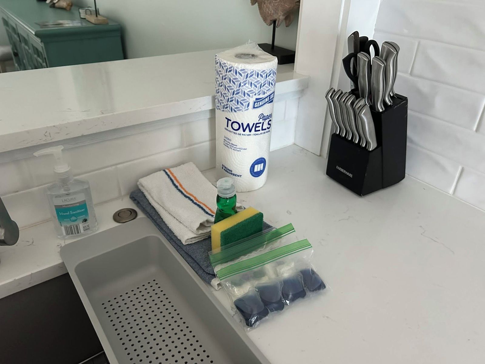 Un lavabo con dispensador de gel antibacterial, una pila de toallas, dispensador de servilletas de papel y un bloque de cuchillos.