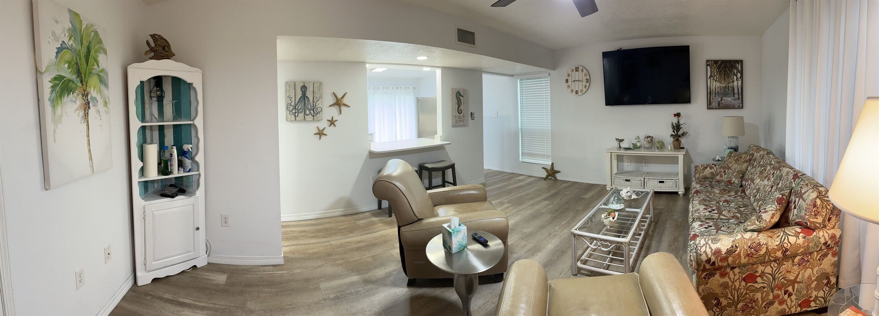Un salon avec un canapé, une table basse et un téléviseur. On y trouve un meuble blanc avec des portes en verre et une décoration en forme d’étoile de mer.