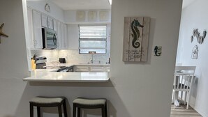 A modern kitchen with white cabinets, a central island, and two stools. - B2 Boujee, a ground floor, cozy condo, just a short walk to the beach.. (Gulf Shores)