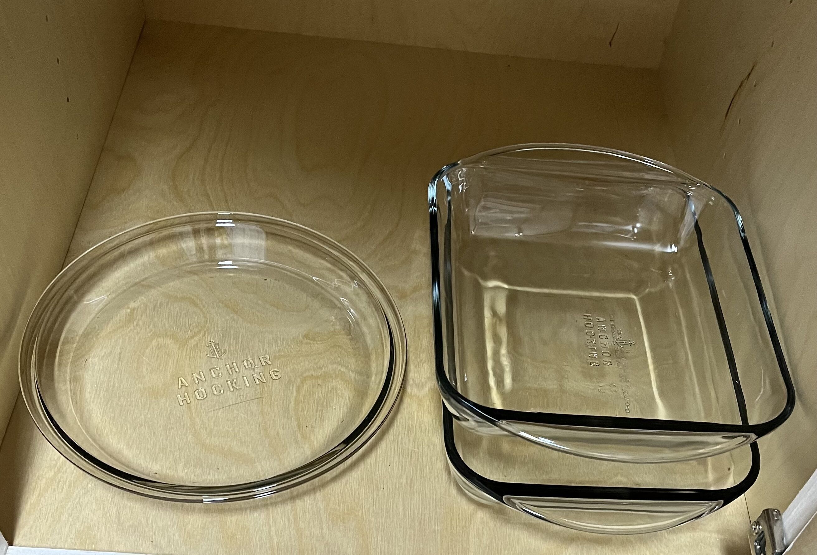 Zwei Glasbackformen mit Deckeln, eine rund, eine rechteckig, in einem Holzkabinent stehen.