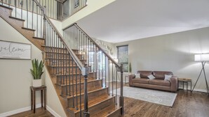 A staircase with wooden steps and metal railings, a brown leather sofa, a white rug, and a potted plant. - Space Command (Colorado Springs)