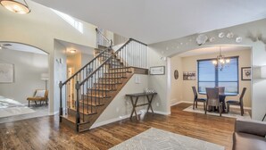 A spacious living area with a wooden staircase, a dining table with chairs, and a chandelier. - Space Command (Colorado Springs)