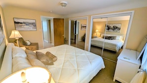 A hotel room with a large bed, a bedside table with a lamp, a chair, and a desk. There is a door leading to another room. - Cozy family retreat (Buffalo)