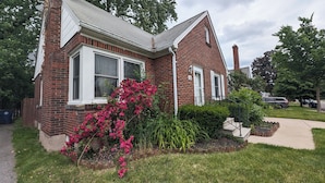 A two-story brick house with a front porch, a small garden with pink flowers, and a visible mailbox. - Cozy family retreat (Buffalo)