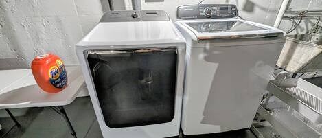 A front-loading washing machine with a control panel, a detergent bottle, and a metal rack.