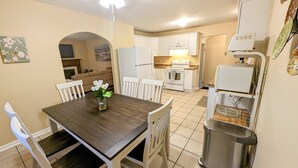 A compact kitchen with white cabinets, a dining table with chairs, and a trash can. - Cozy family retreat (Buffalo)