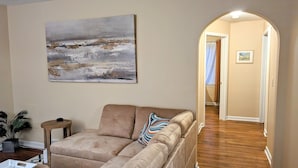 A living room with a beige sofa, a small round table, a potted plant, and a painting on the wall. - Cozy family retreat (Buffalo)