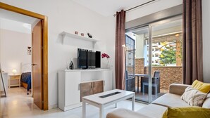 Ein modernes Wohnzimmer mit einer Couch, einem Couchtisch, einem Fernseher auf einem weißen Schrank und einem Balkon mit Blick nach außen.