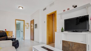Ein modernes Wohnzimmer mit einem weißen Sofa, einem weißen Couchtisch, einem Fernseher auf einem weißen Schrank und einer Holztür.