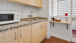A kitchen with wooden cabinets, a white microwave, a double sink, and a window with blinds.