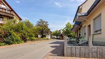 En gatubild med ett kafé som heter ”Café Leins” på höger sida, en byggnad med en balkong på vänster sida och en klar himmel.