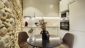 A modern kitchen with white cabinets, a stone wall, a round table with chairs, and a vase with flowers. - Apartamento de una Habitación Vistas al río Onyar (Girona)