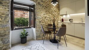 A modern kitchen with stone walls, a dining area with a table and chairs, a potted plant, and a view of a building through a window. - Apartamento de una Habitación Vistas al río Onyar (Girona)