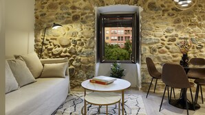 A cozy room with a stone wall, a sofa, a dining table with chairs, and a window with a view of buildings. - Apartamento de una Habitación Vistas al río Onyar (Girona)