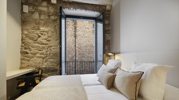 A bedroom with a stone wall, a bed with white bedding, a desk, and a chair. - Apartamento de una Habitación Vistas al río Onyar (Girona)