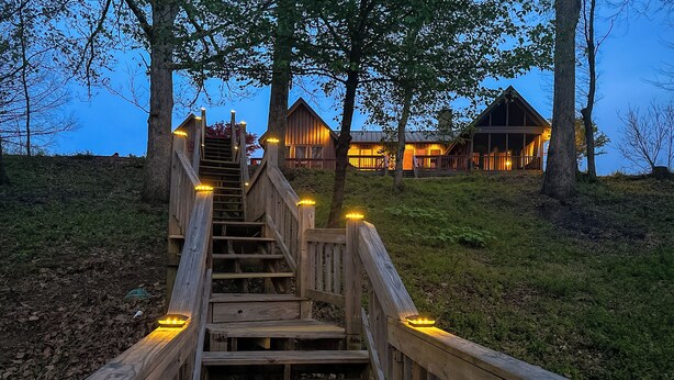 A wooden staircase leading to a lodge with multiple wooden buildings, surrounded by trees. - Riverfront Bliss- Private River Dock & Two King rooms! (Pangburn)