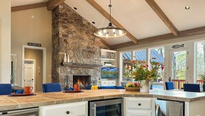 A modern kitchen with a stone fireplace, a large island with seating, and a view of the outdoors. - Riverfront Bliss- Private River Dock & Two King rooms! (Pangburn)