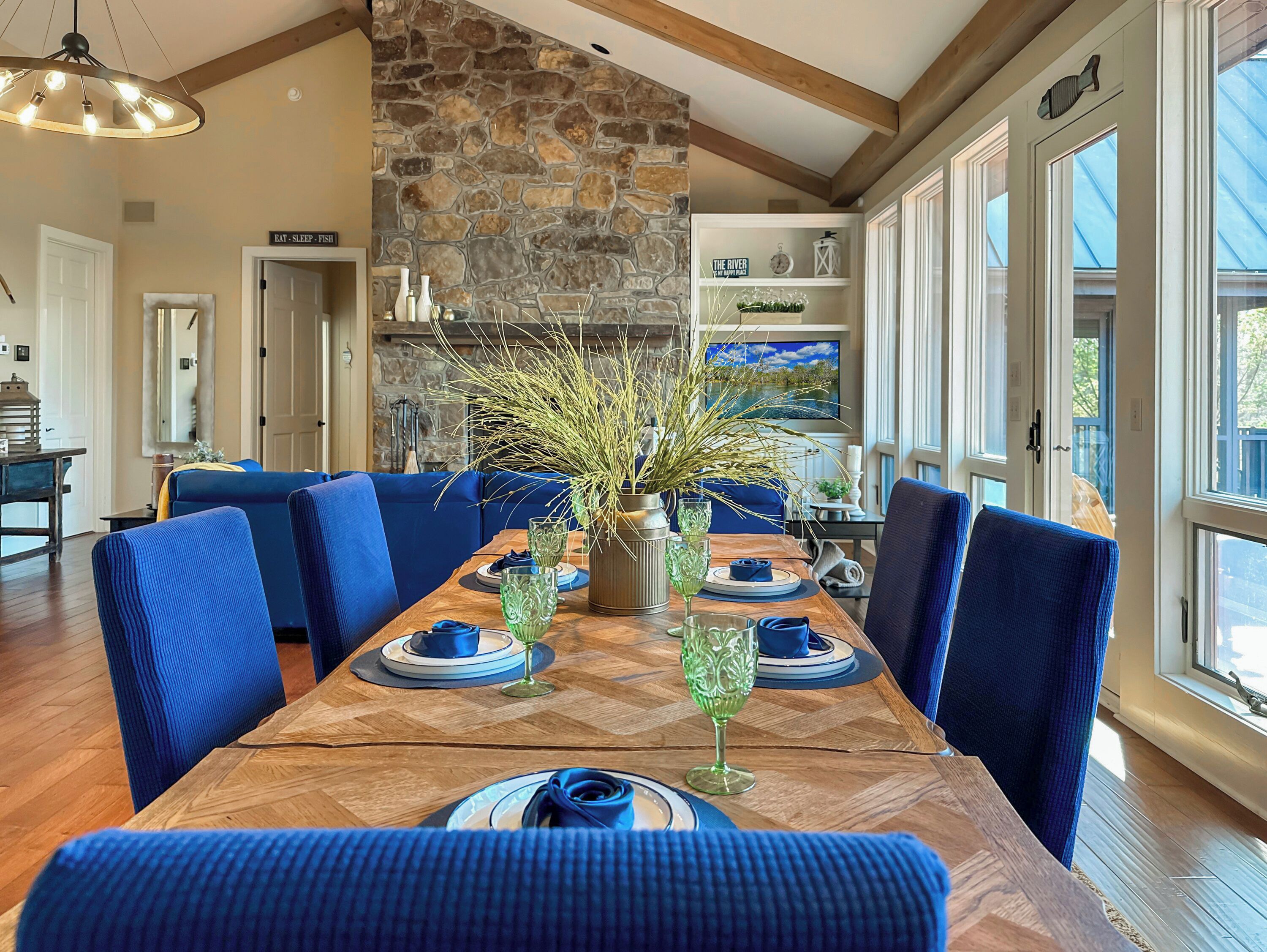 Un espace repas avec une longue table en bois, des chaises à l’assise rembourrée de tissu bleu et un mur en pierre.