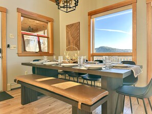 Uma sala de jantar com uma mesa comprida posta para quatro pessoas, cadeiras de madeira e um banco.