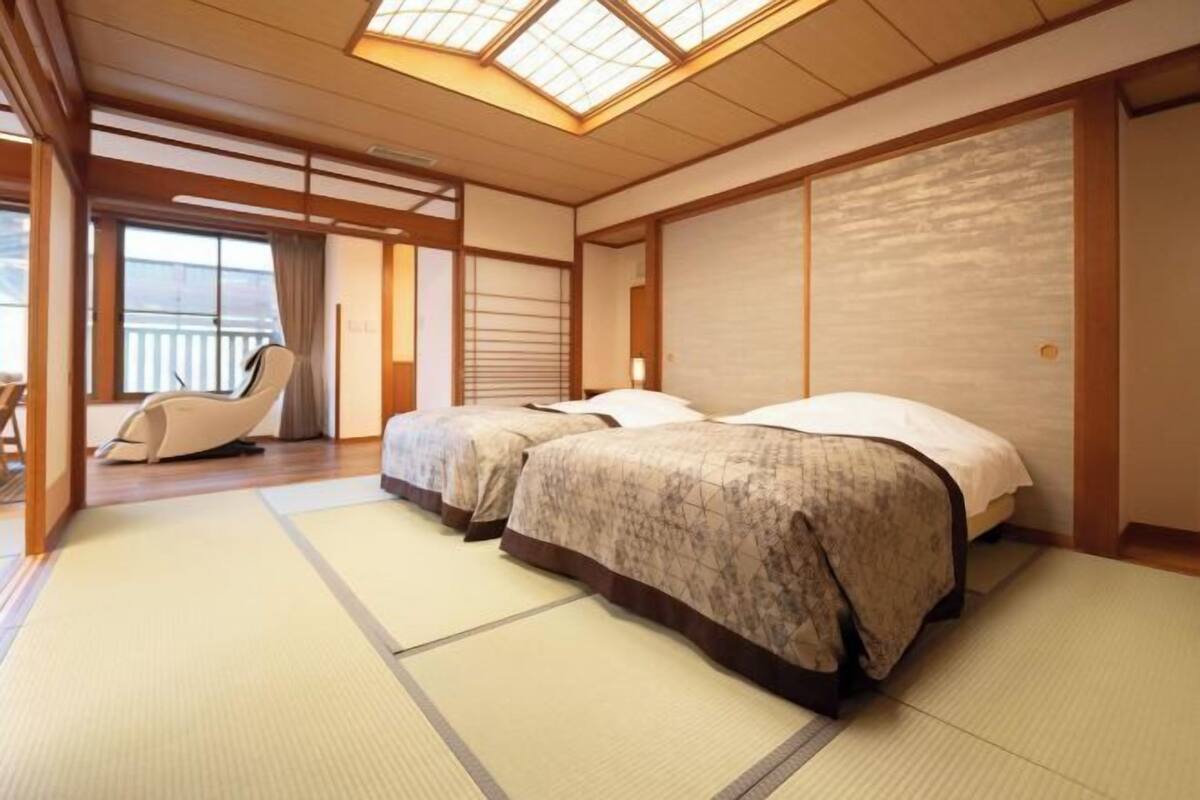 A traditional Japanese-style room with tatami flooring, two beds, a sliding door, and a view of the outside.