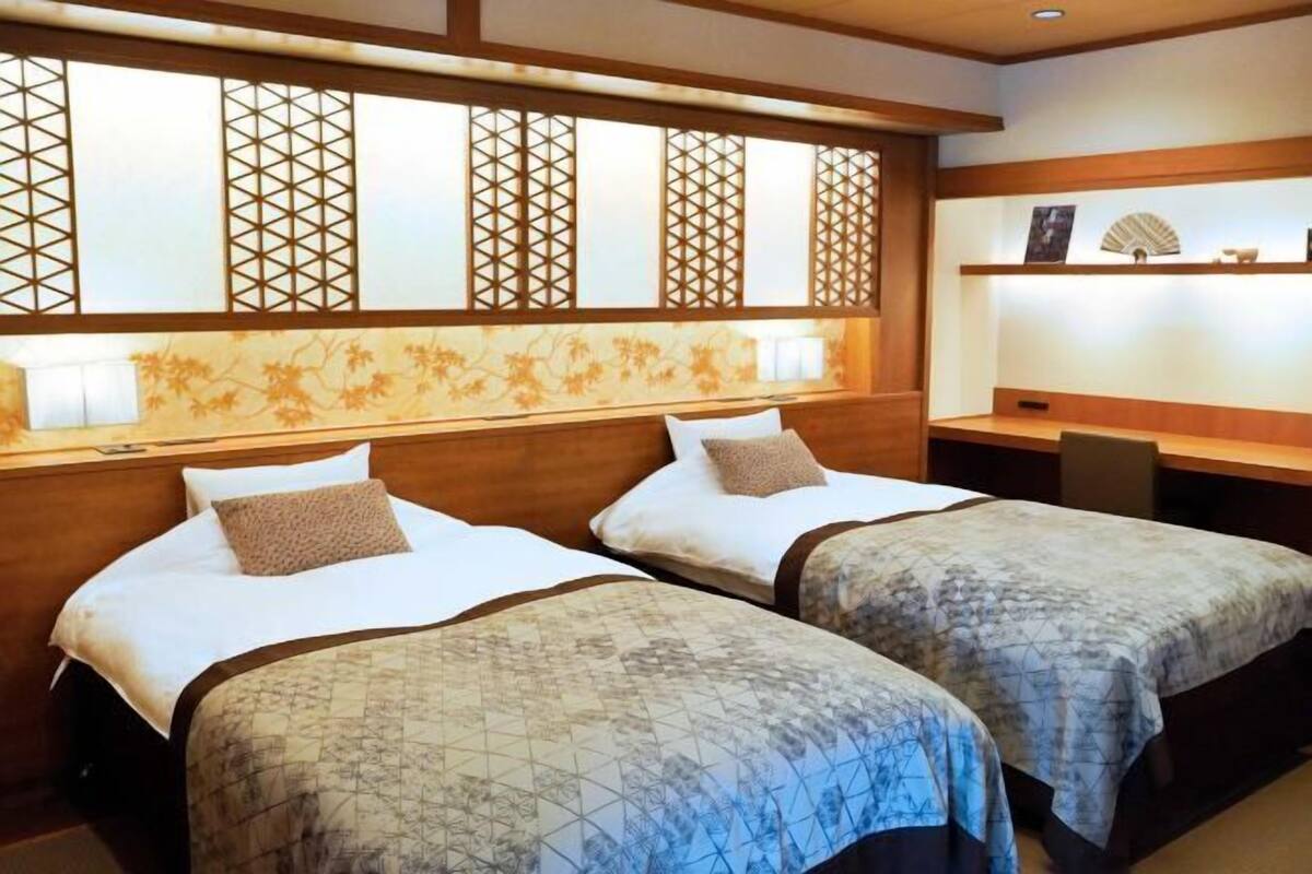 A hotel room with two beds, a wooden headboard, a desk, and a decorative wall with a lattice design.
