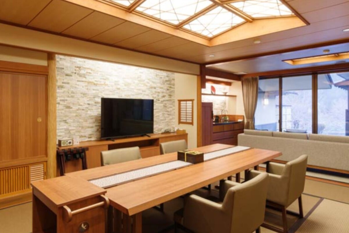 Una habitación tradicional japonesa con una mesa de comedor de madera, sillas, un televisor y una pared de piedra.