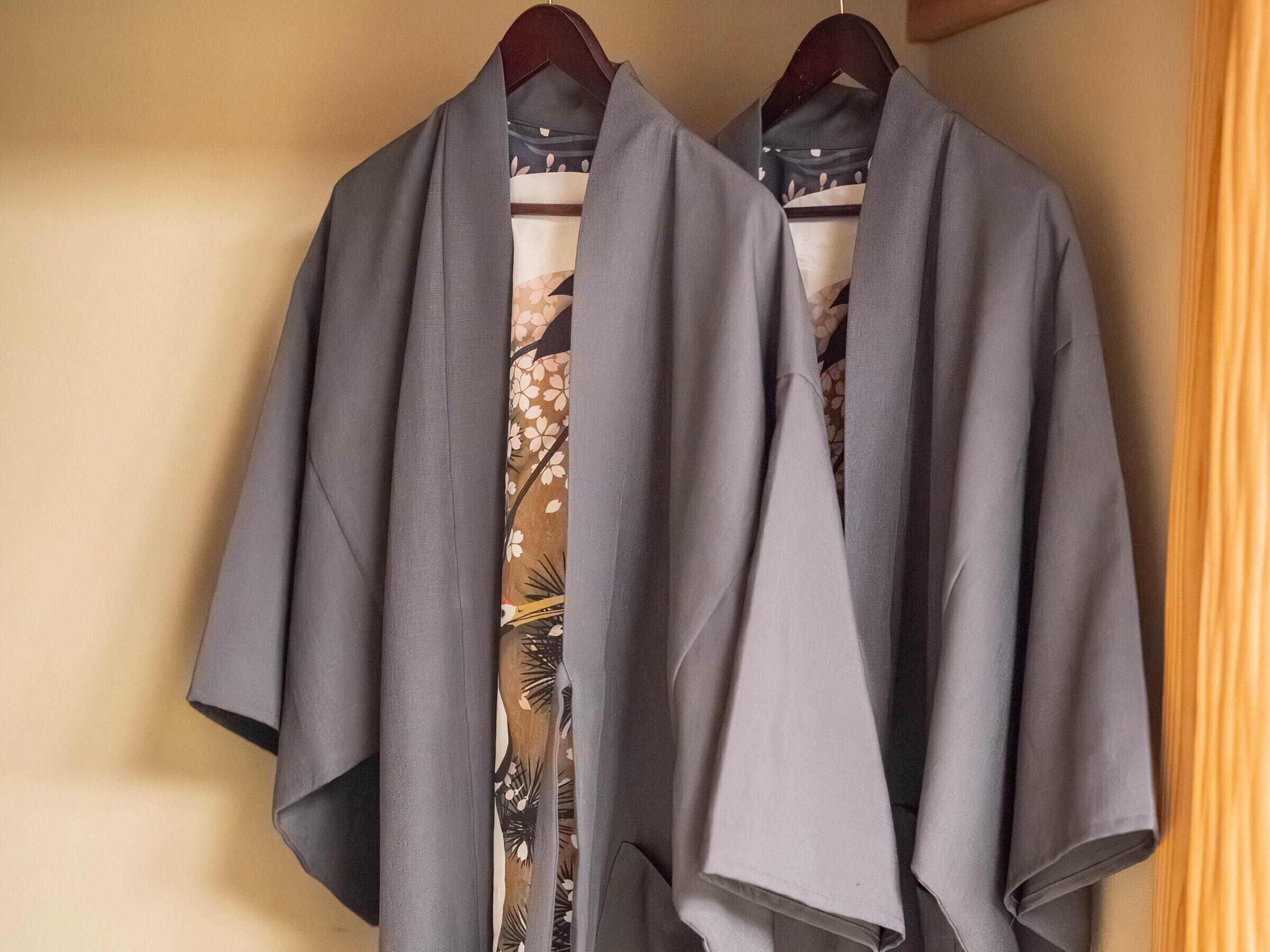 Two grey robes hanging on a wooden hanger against a beige wall.