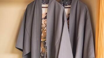 Two grey robes hanging on a wooden hanger against a beige wall.