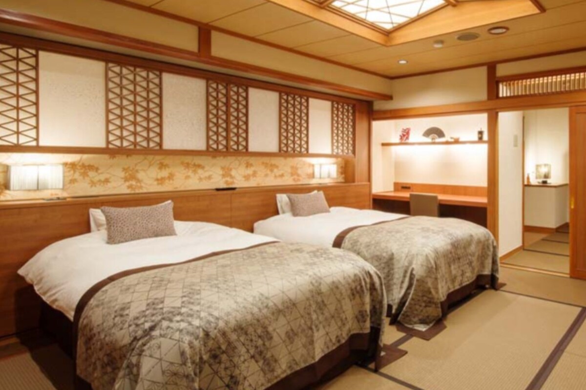 A traditional Japanese-style hotel room with two beds, tatami flooring, and a sliding door.