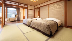 Une pièce de style japonais traditionnel, avec un sol recouvert de tatamis, deux lits dotés de draps à motifs, une porte coulissante et une vue sur un bâtiment à l’extérieur.