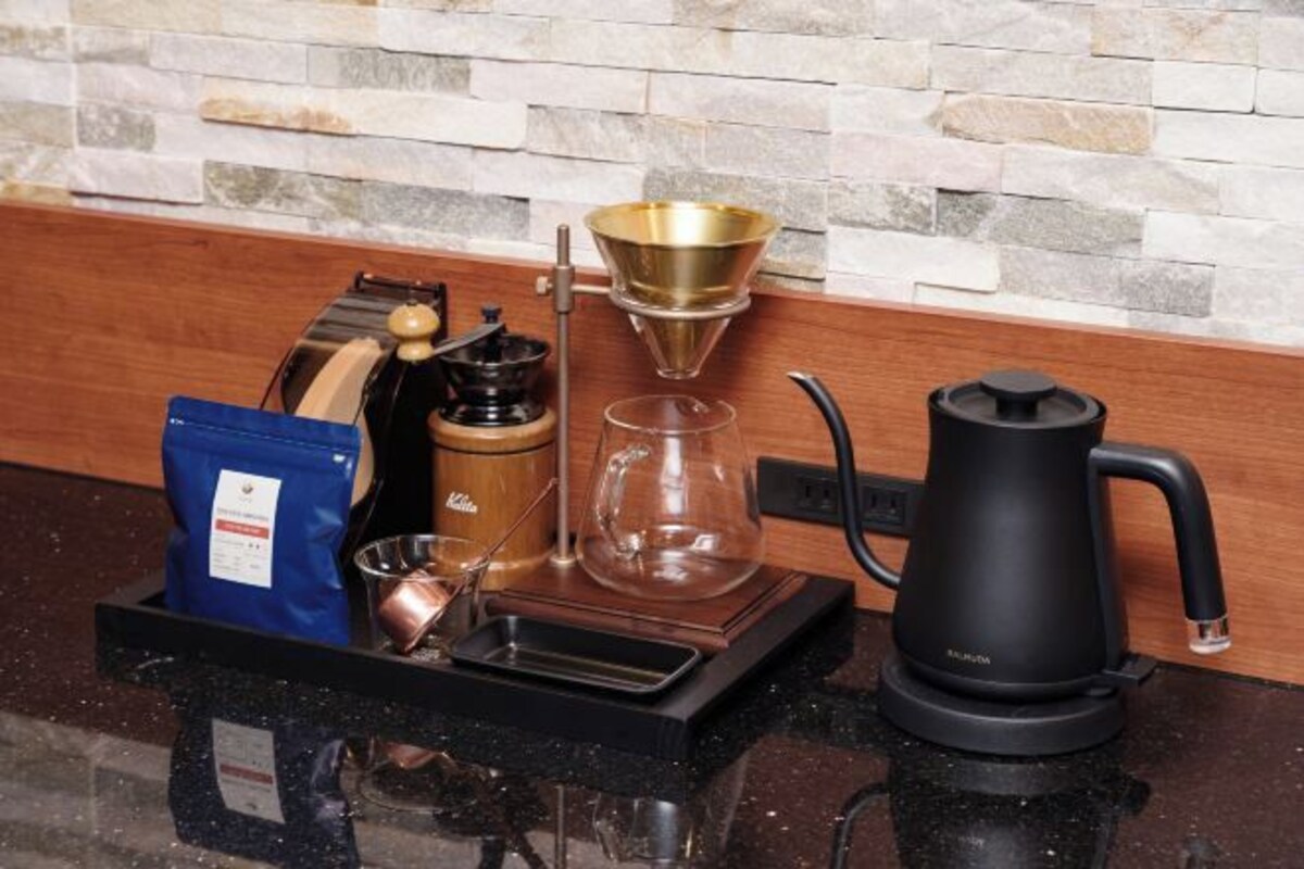 Una cafetera, una jarra de vidrio, una tetera de metal, un paquete de café y una tetera sobre una encimera.
