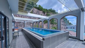 Un espace piscine aménagé sur le toit, offrant une vue sur une falaise rocheuse, un coin salon abrité et une entrée avec porte vitrée.