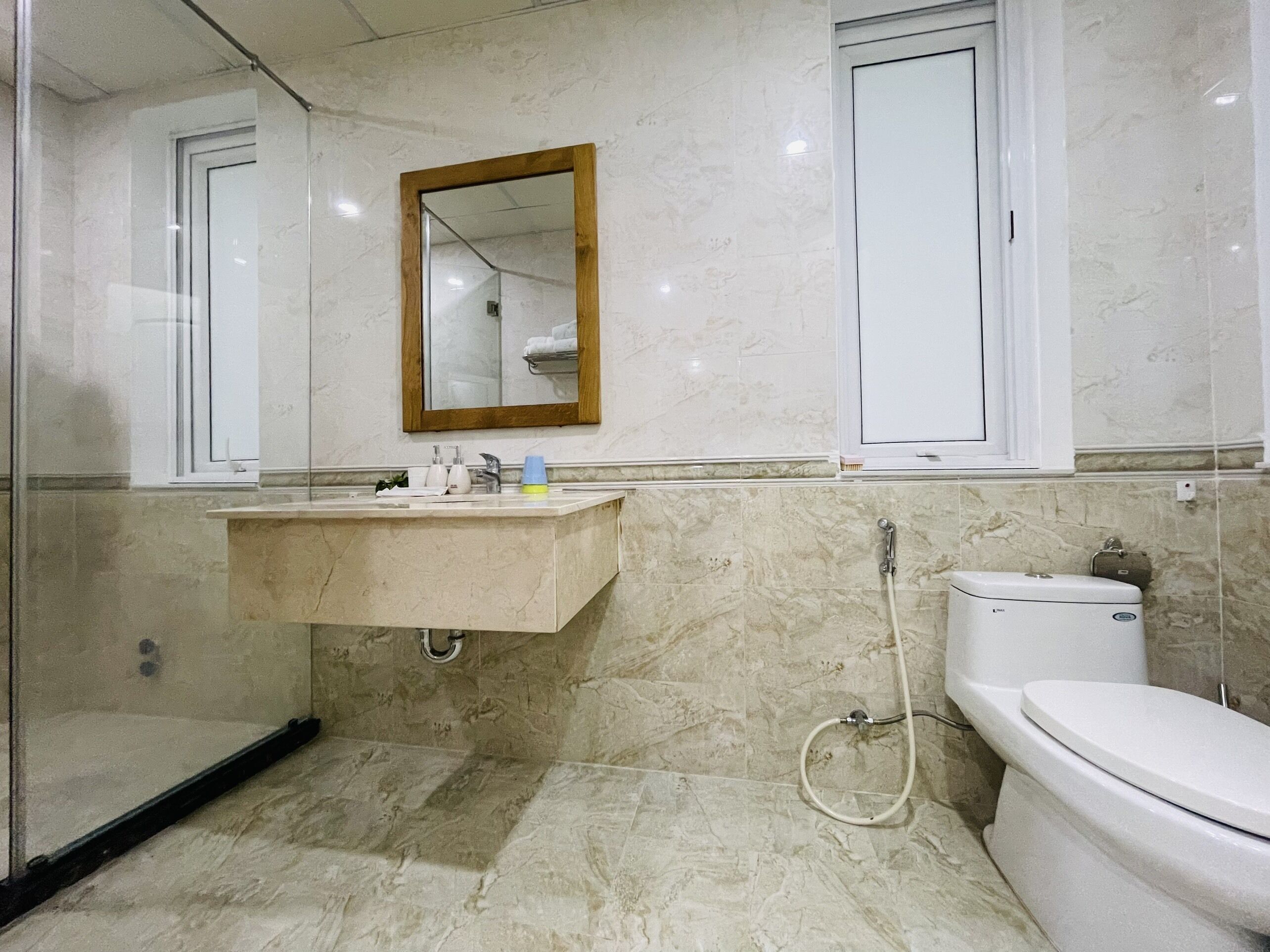 A bathroom with a marble floor, a sink with a mirror above it, a toilet, and a shower.