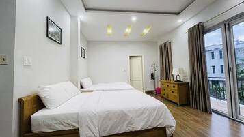 A modern hotel room with two beds, a wooden dresser, a coat rack, and a large window with a view of buildings.