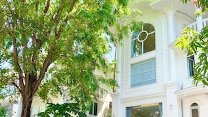 Une voiture noire est garée devant un bâtiment blanc, avec un grand arbre au premier plan.