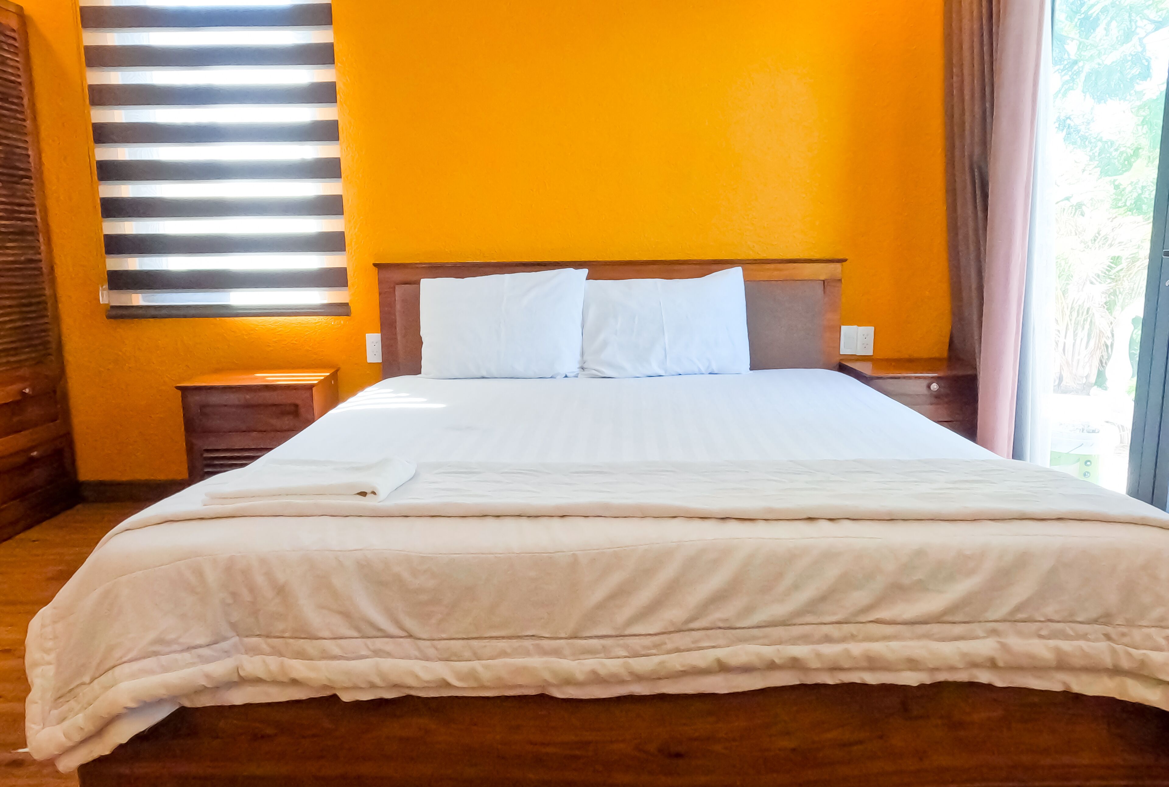 Una cama bien hecha con sábanas blancas en una habitación con paredes anaranjadas y un cabecero de madera.