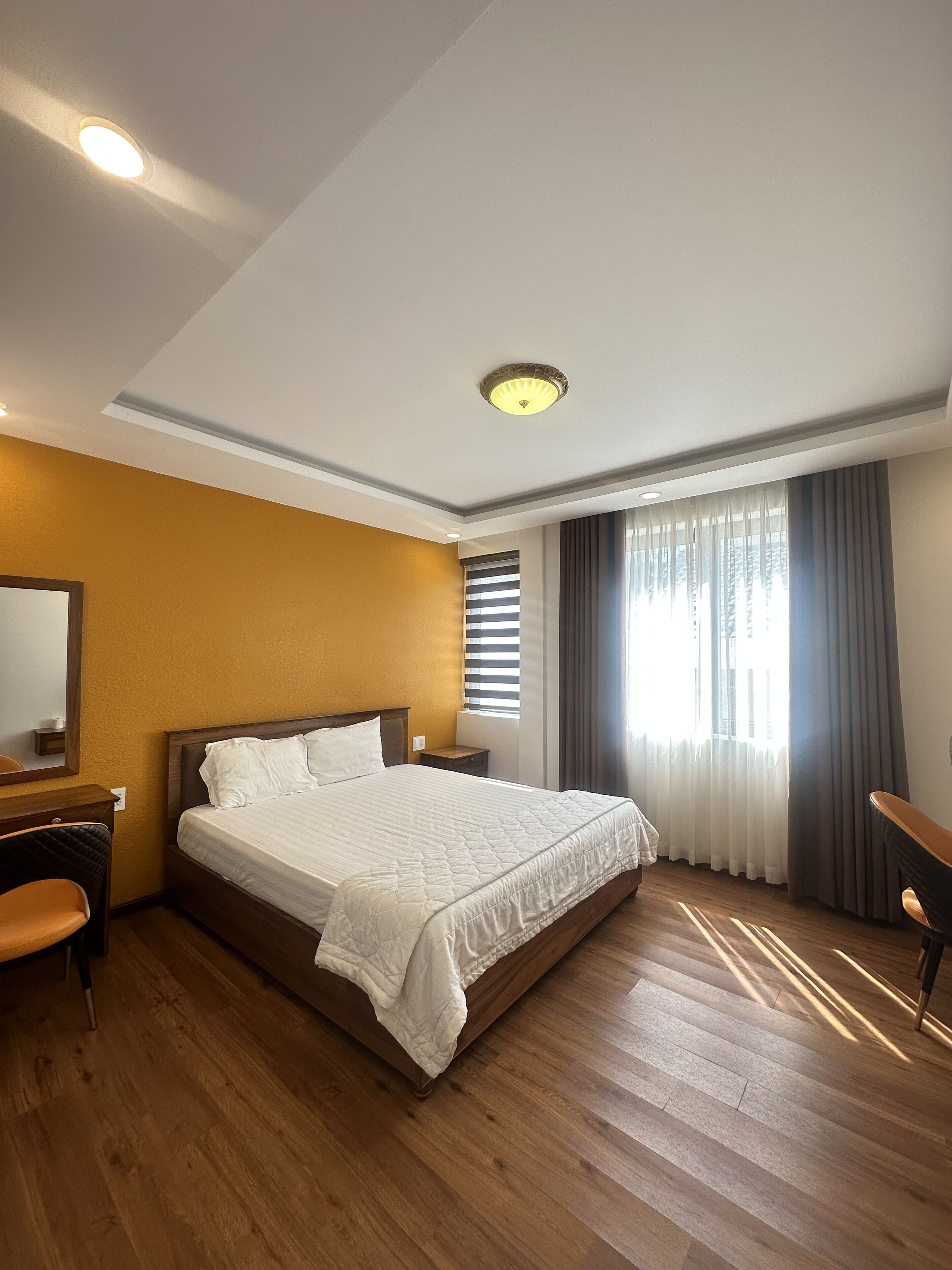 Une chambre d’hôtel avec un grand lit, un plancher en bois, un bureau et une fenêtre avec des rideaux.