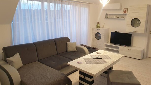 Ein modernes Wohnzimmer mit Ecksofa, Couchtisch, Flachbildfernseher und einer kleinen weißen Kommode.