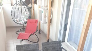 Ein Balkon mit Korbmöbeln, einem roten Stuhl und einem Glastisch.