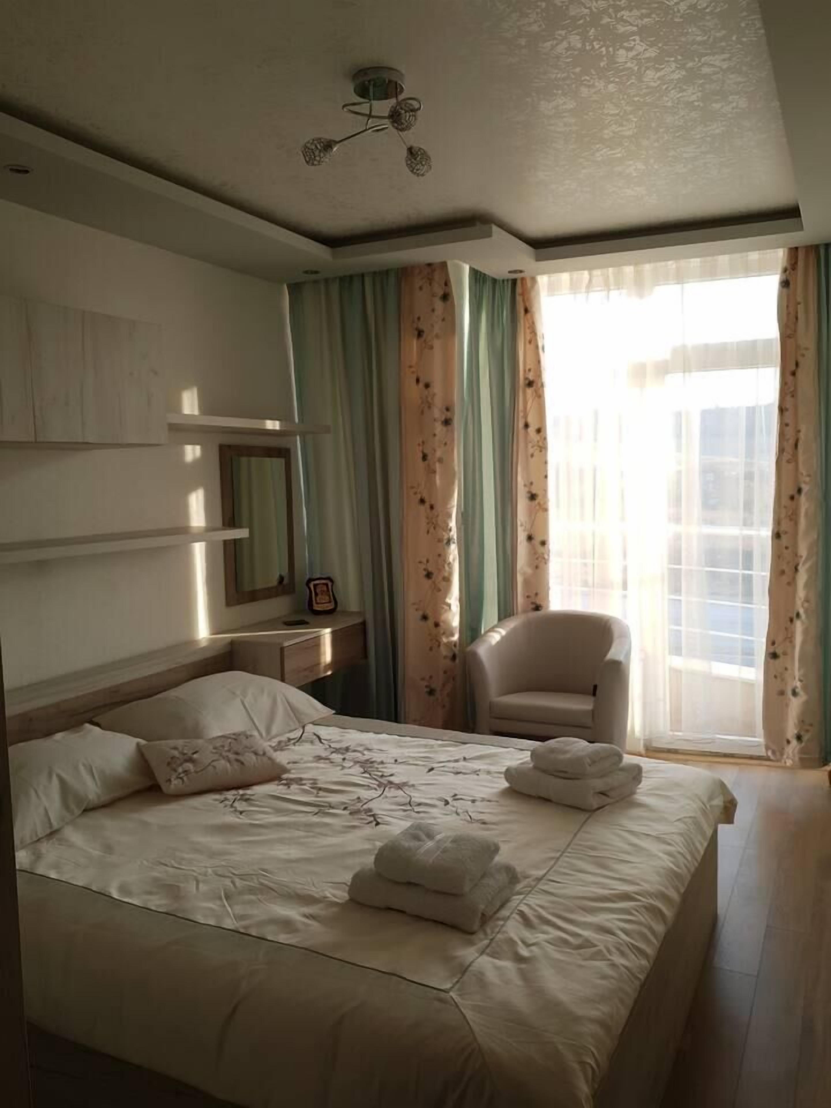 Une chambre d’hôtel avec un grand lit, une chaise, un bureau et une fenêtre avec des rideaux.