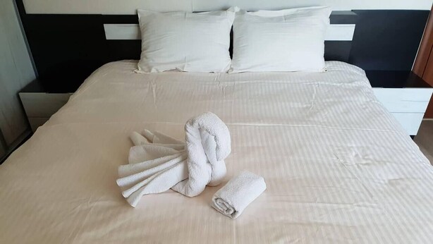A neatly made bed with a folded towel and a rolled towel on a light-colored bedspread.