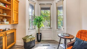 A corner room with a bay window, a wooden cabinet, a potted plant, a wicker basket, and a small table with a chair. - ☆New! Central+FreeParkin+GYM+Kingbed (Pittsburgh)