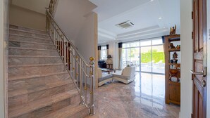 Un amplio salón con una escalera de mármol, un gran ventanal con vistas al exterior y un aparador de madera con adornos.