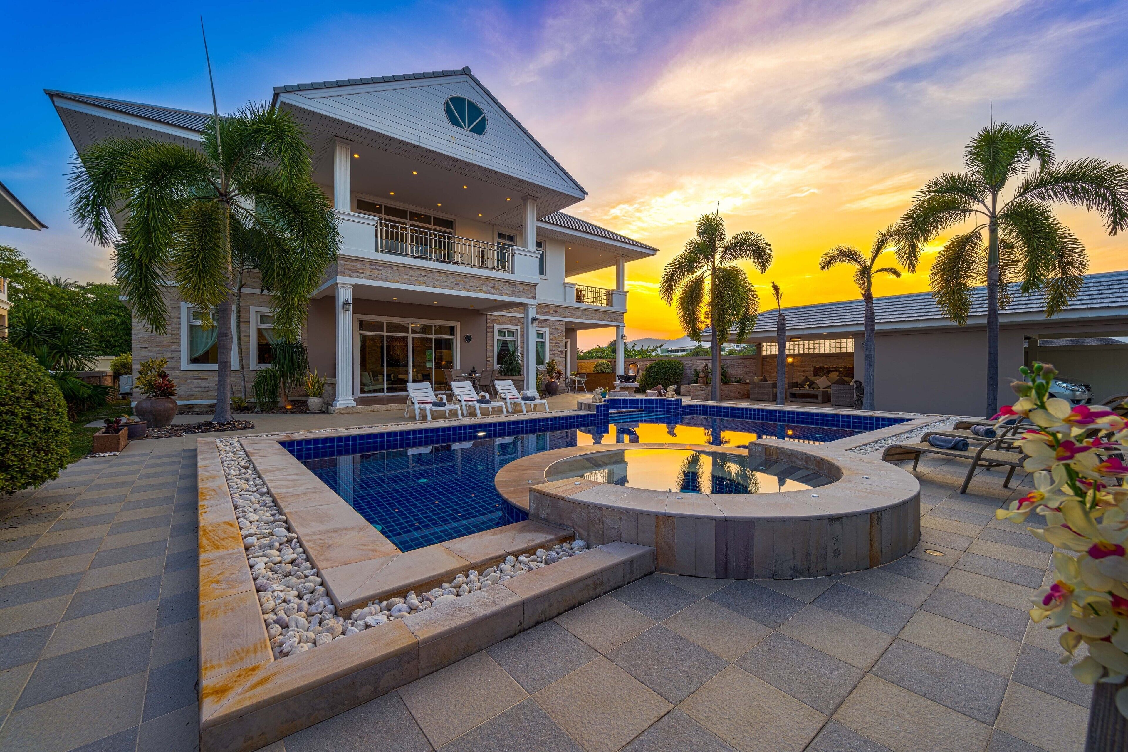 A modern house with a swimming pool, a hot tub, and a patio area with lounge chairs.