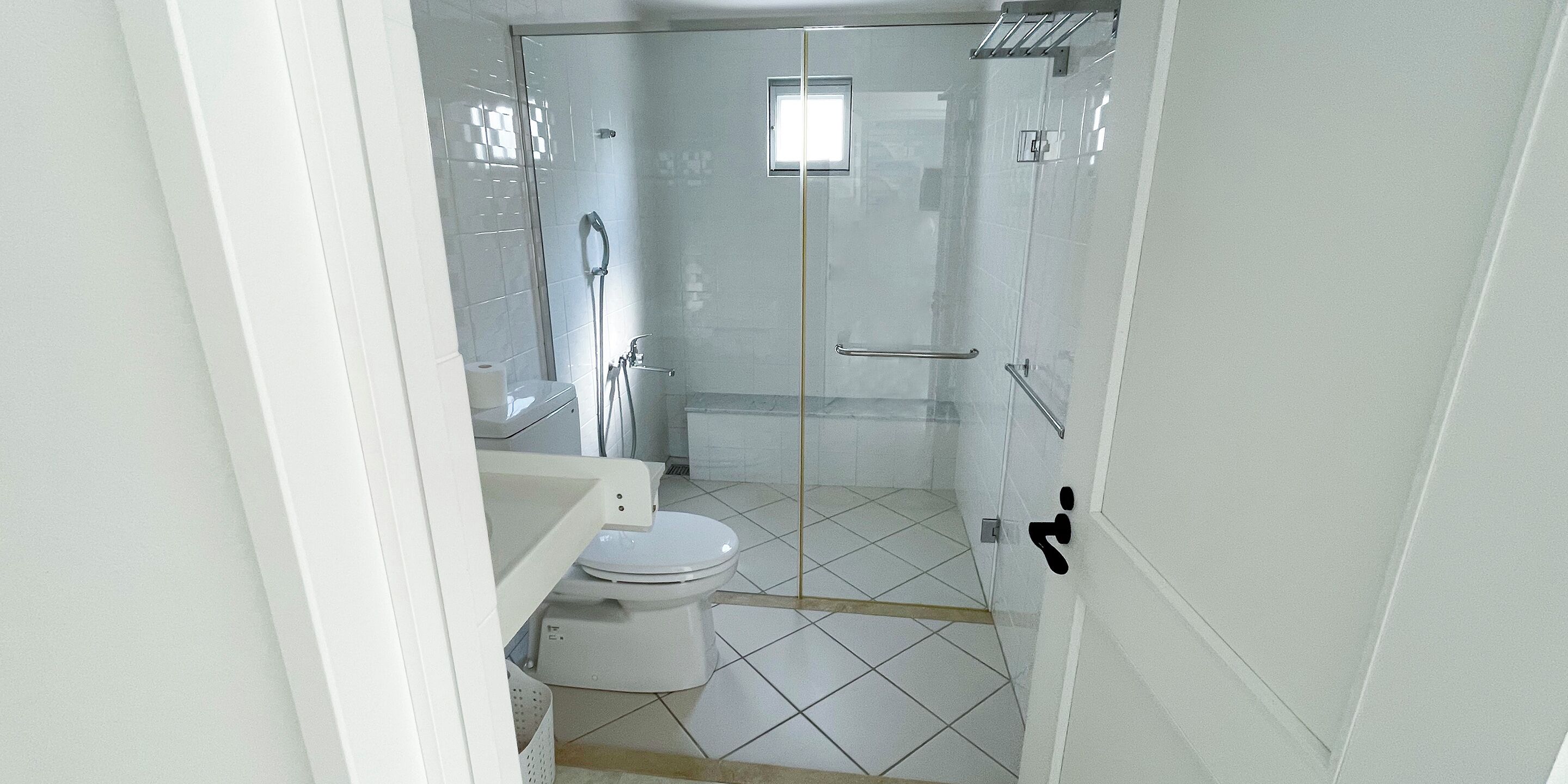 A modern bathroom with a glass-enclosed shower, white tiles, and a visible toilet.