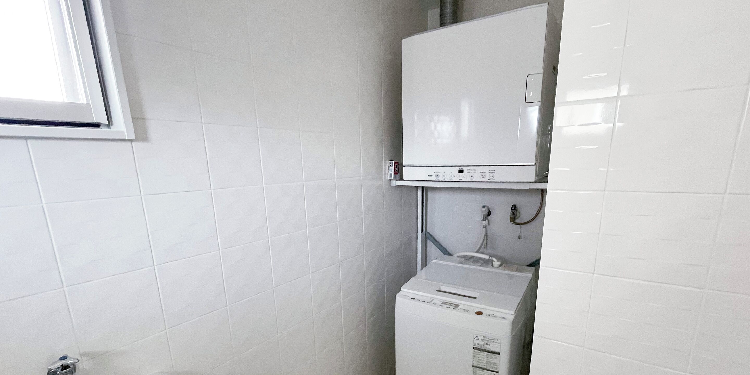 A small, clean room with white tiled walls and a white washing machine.