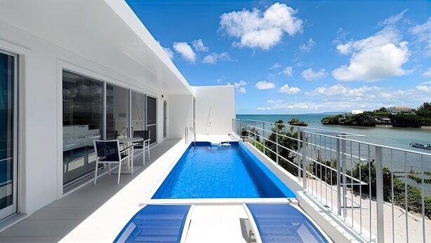 Un balcón moderno con piscina, puertas de cristal y vista al mar.