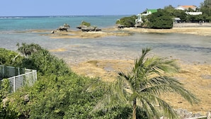 Una playa con agua cristalina, rocas y un edificio blanco con techo verde.