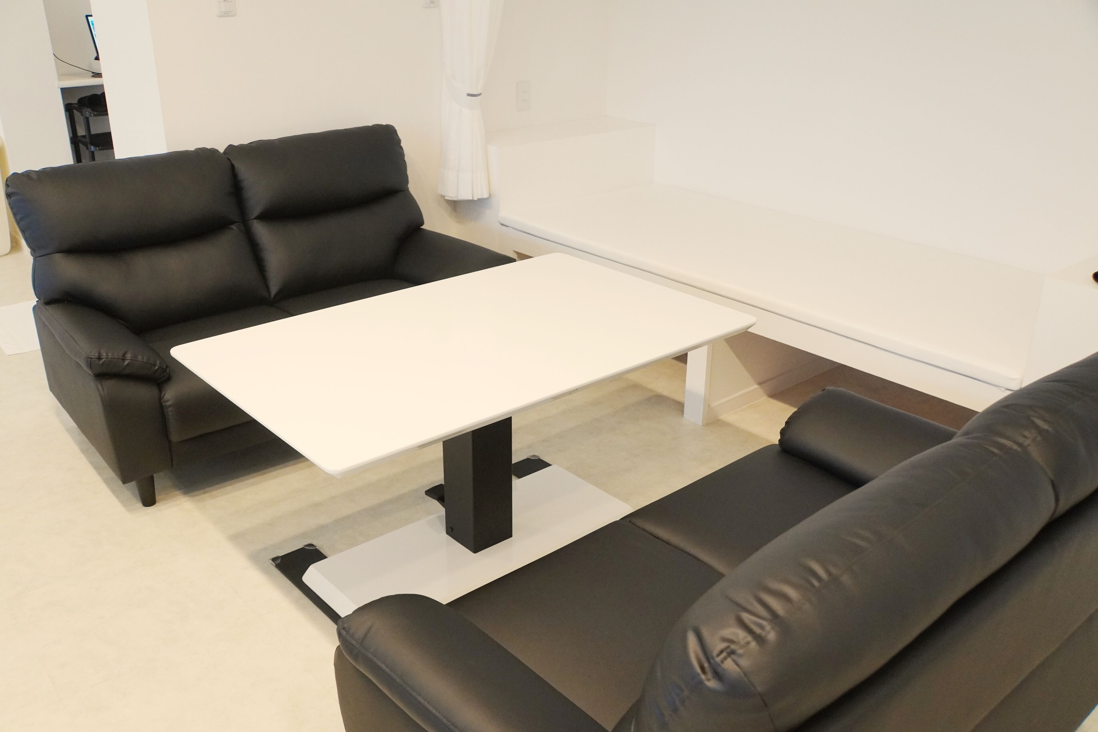 A modern living room with a black leather sofa, a white coffee table, and a black leather couch.