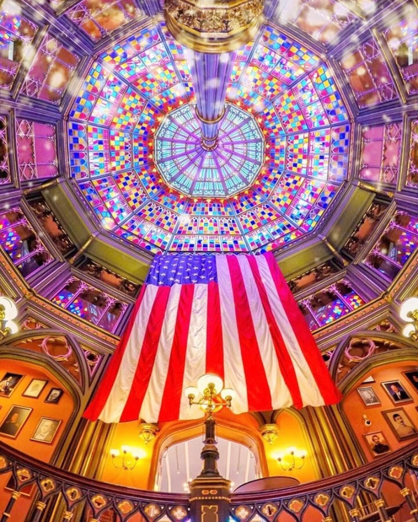 Un salón imponente con un techo de vidrieras grande y de colores vivos, y una bandera estadounidense colgando del techo.